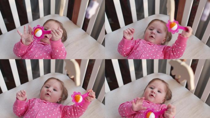 可爱快乐的女婴，穿着粉色连体衣，戴着玩具拨浪鼓，在阳光明媚的早晨在室内玩得很开心