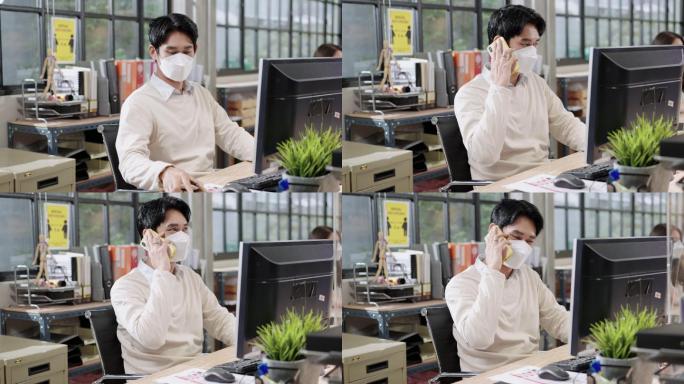 新常态的环境在现代办公室工作带有2019冠状病毒疾病，亚洲商人通过屏幕分隔与客户和朋友打电话做生意，