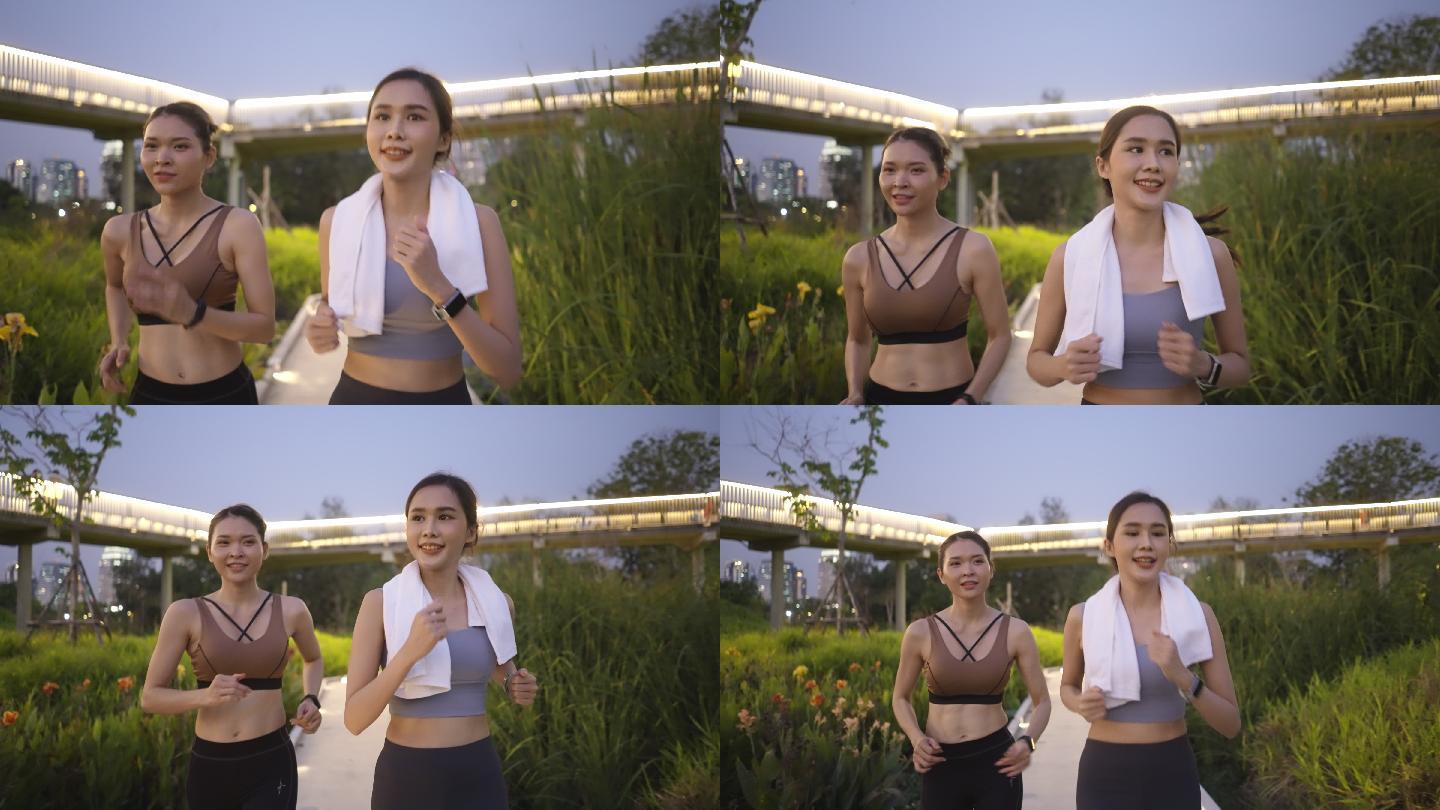 正面图：两位亚洲美丽的中年女性朋友穿着运动装，肌肉发达，在黄昏时分一起积极慢跑，使用智能手表监控，在