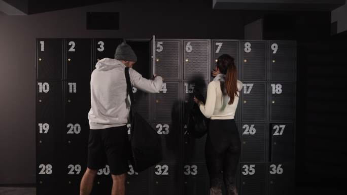 两名运动员在健身房把包放进储物柜时的后视图