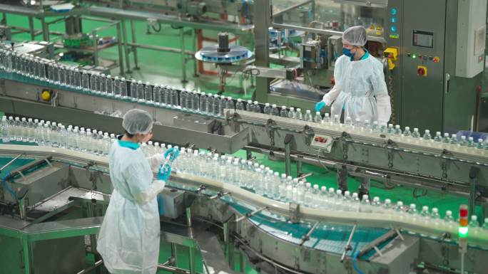 2名中国亚裔饮用水厂生产线工人，戴着个人防护用品，在日常工作中检查水瓶