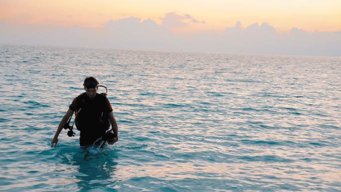 日落时分，戴着水下呼吸器的潜水员走出海洋来到海滩上