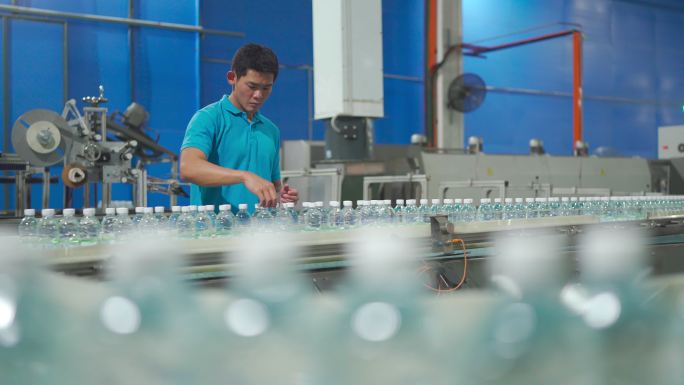 中国亚裔男性生产线工人在瓶装厂矿泉水饮用水厂检查水瓶