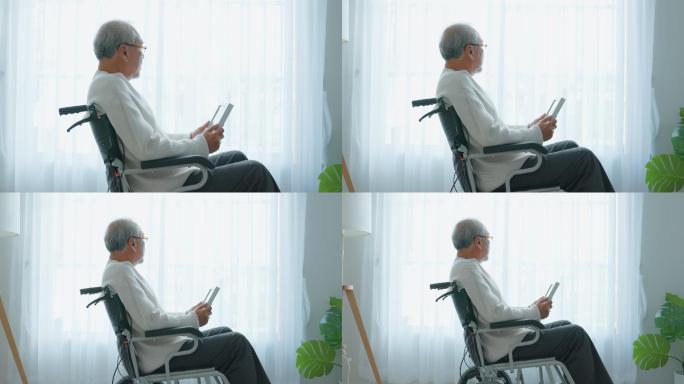 亚洲老年男性独自坐在轮椅上看家庭照片。年迈、成熟的祖父感到孤独和悲伤，退休后留在养老院思念亲人和妻子