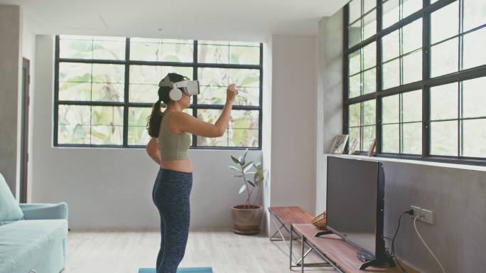 年轻运动女性佩戴VR耳机体验模拟数字世界在家客厅锻炼