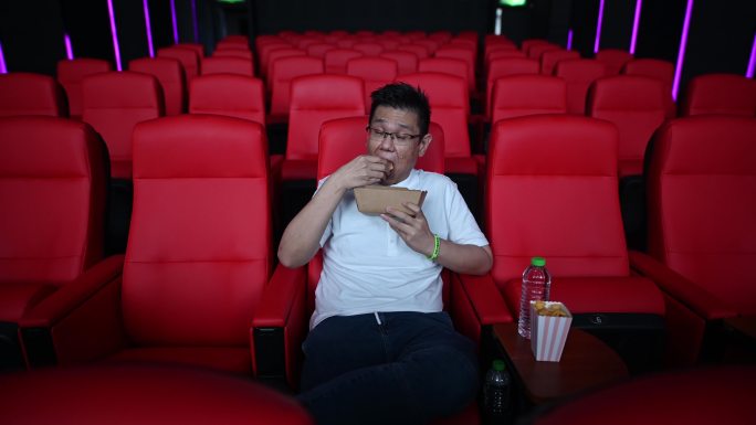 亚裔中国成年男子独自在电影院看电影，一边吃零食