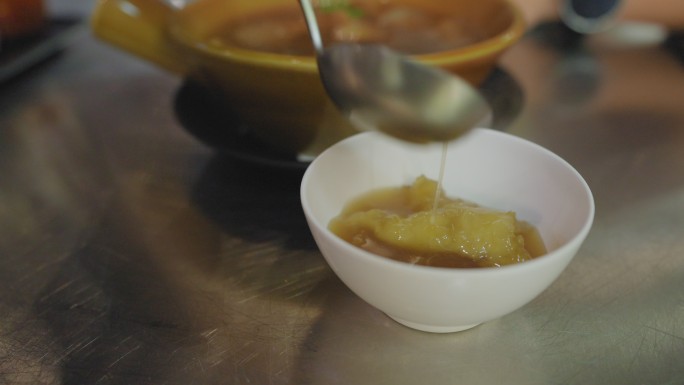曼谷唐人街Yaorawat的一家街头美食餐厅，在金属桌上用塑料汤匙分享碗里的热鱼肚汤。黑胡椒女调味品