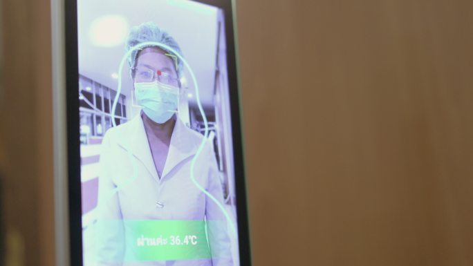 封闭式护士走向摄像头，在智能触摸屏温度计上聚焦和测量她的体温-库存视频