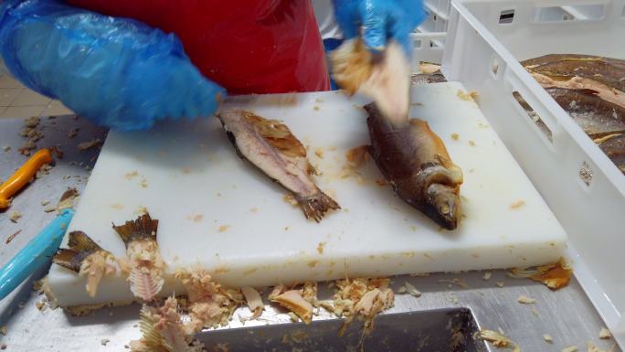 一名工人正在一家工业鱼类包装设施中用鱼片刀清理菲力鲑鱼和鳟鱼的包装