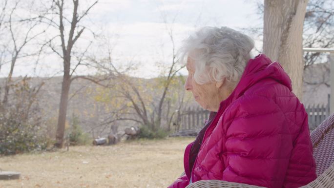 一位100岁高龄女性的侧面照片，她在冬天坐在户外，俯身向前看