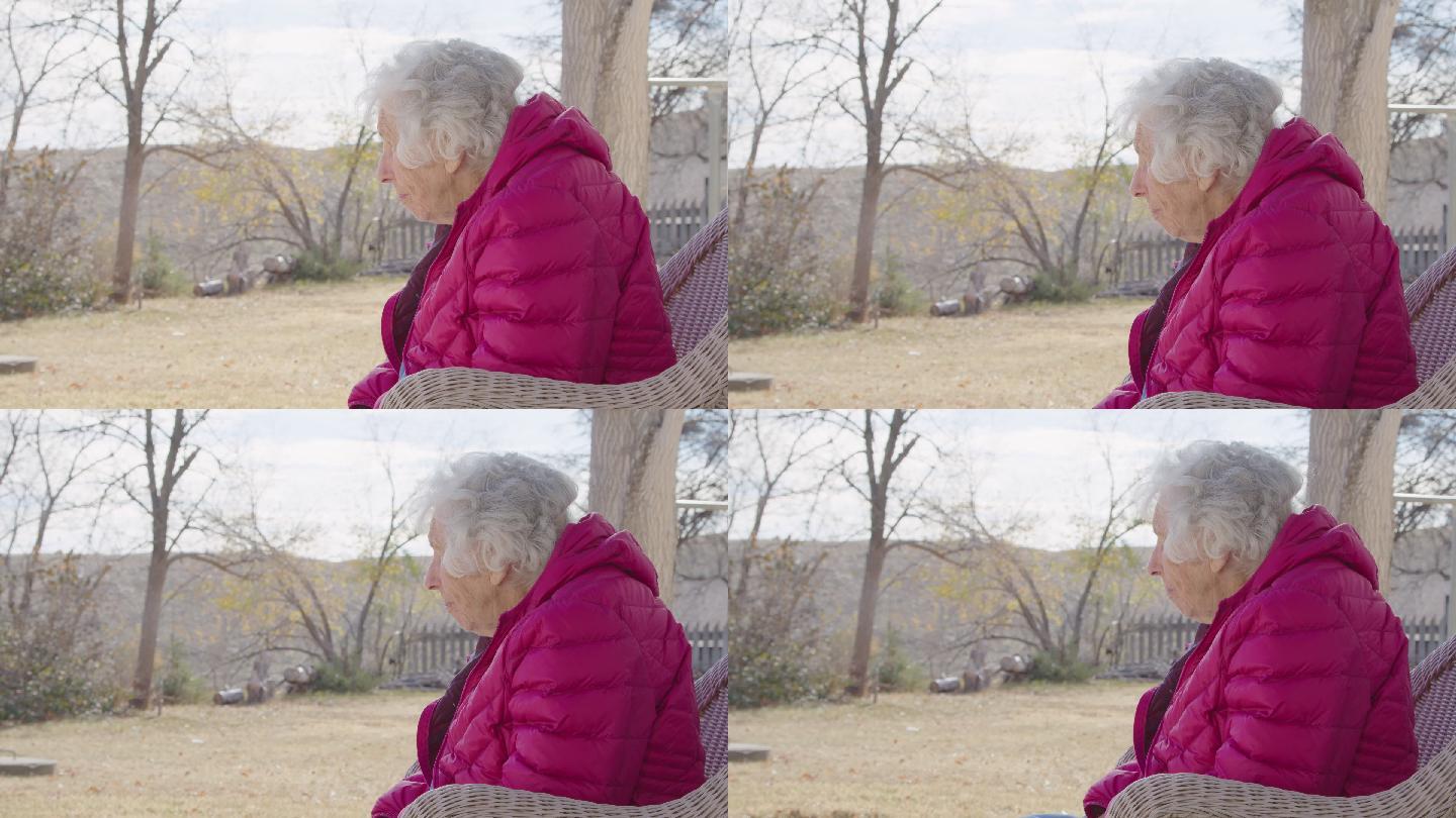一位100岁高龄女性的侧面照片，她在冬天坐在户外，俯身向前看
