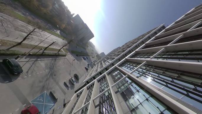 360度视图。蓝天映衬下的现代玻璃建筑的城市景观。FPV无人机向上和内部飞行
