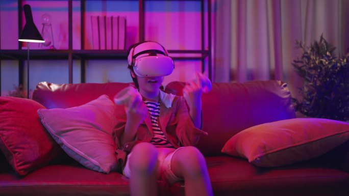 隔离期内，亚洲男童戴着VR或虚拟现实眼镜，戴着耳机，站在起居室电视机前玩视频游戏