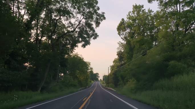 日落时分，在宾夕法尼亚州巴洛附近的一条绿树成荫的道路上开车