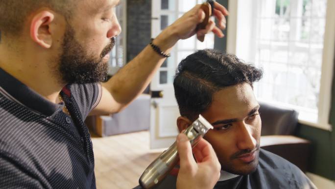 理发师在理发店用电动剃须刀刮男人的头发