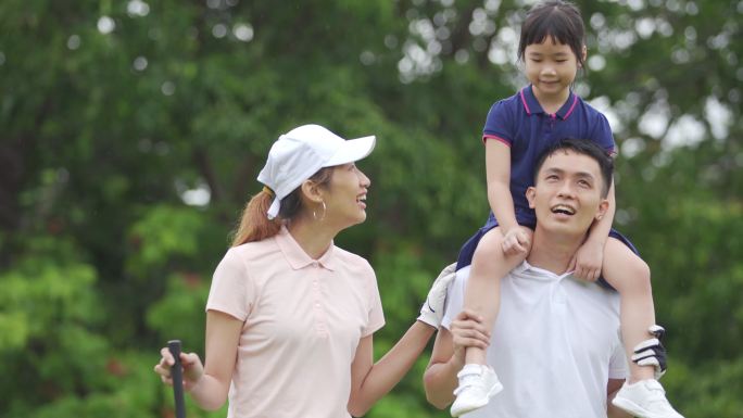 快乐的亚裔中国高尔夫夫妇与女儿在高尔夫球场建立友谊