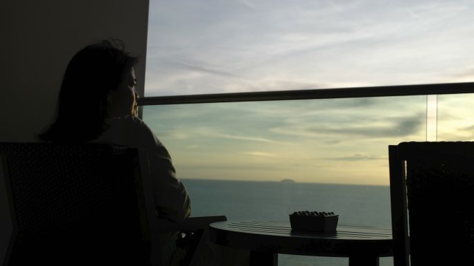 剪影女子坐在露台上，在海上度假室里看着日落