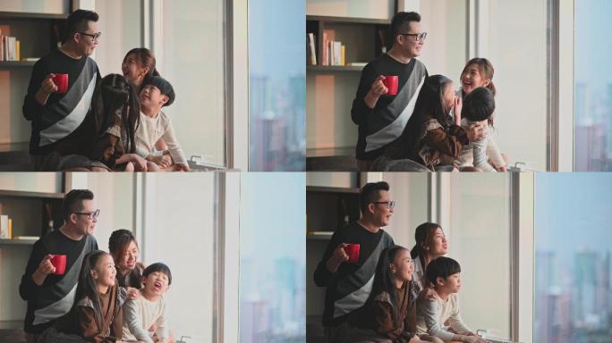 吉隆坡cit，一个亚裔华人家庭和两个孩子透过窗户在客厅欣赏美丽的日落
