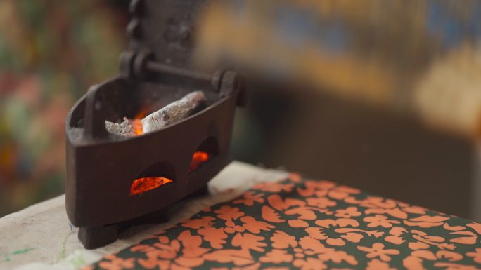 特写亚裔中国高级女裁缝在工作室熨布前扇动古董熨斗加热