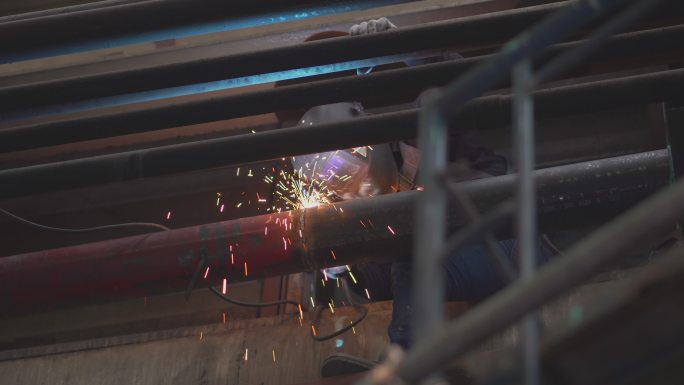技师用焊接气体切割金属，打磨金属切割过程中掉落在地板上的金属火花，在工厂内努力高空拆除金属结构