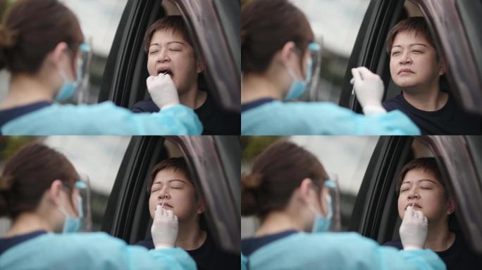 在停车场的室外，亚裔中国女医生带着PPE从患者冠状病毒试验中取鼻拭子。防护套间的医务人员正在用拭子进