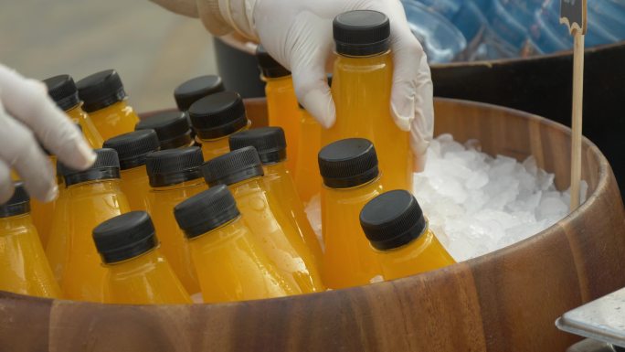 双手将橙汁瓶放在木制冰桶中，以便在市场上销售。
