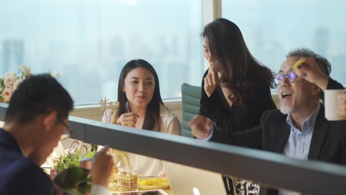 一群亚裔中国白领在工作时间休息到很晚，并在工作站办公室工作地点吃零食