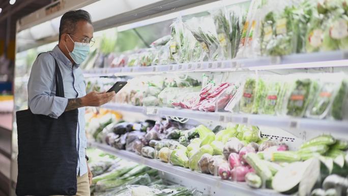 亚裔中国老人戴着口罩在超市蔬菜冷藏区购物