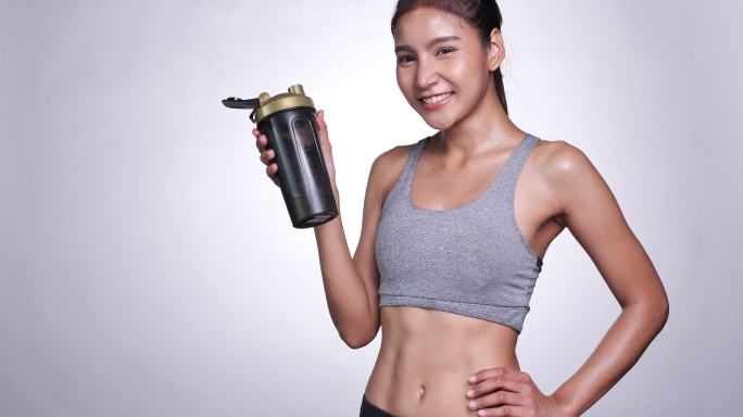 白人背景的年轻亚洲女性饮用乳清蛋白补充剂以保持健康并控制饮食。