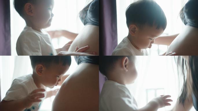 男孩在卧室里与怀孕的妈妈肚皮玩耍亲吻