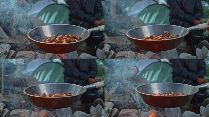 篝火上摇动烤栗子的慢炖锅