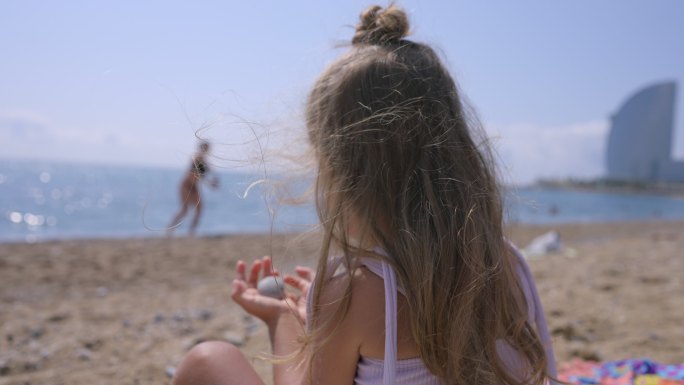 巴塞洛塔海滩上穿着比基尼的小女孩在玩石头