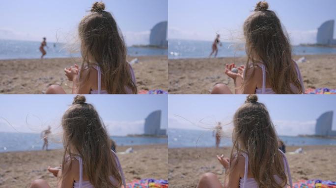 巴塞洛塔海滩上穿着比基尼的小女孩在玩石头