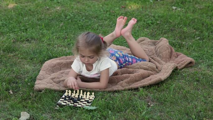 孩子躺在草坪上的毛皮大衣上整理棋子