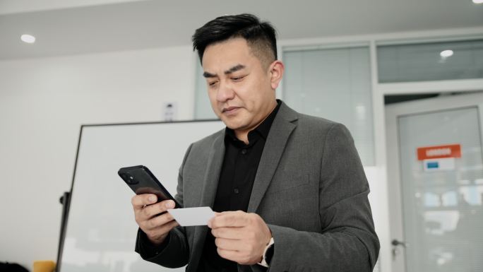 一位亚洲商人在一个合作空间持有智能手机信用卡。