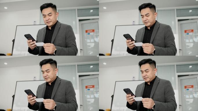 一位亚洲商人在一个合作空间持有智能手机信用卡。