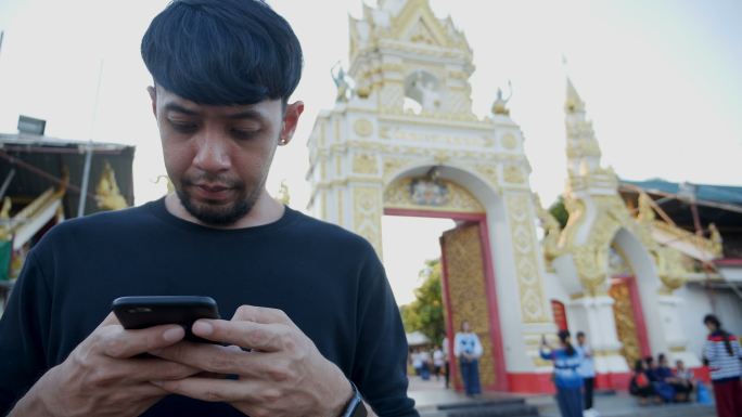 年轻的亚洲男子使用手机触摸屏和通话。在temple的背景下打电话。概念：新商务、旅游、通讯。