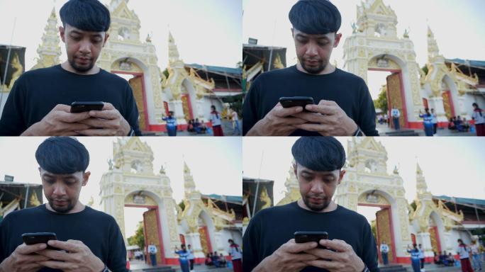年轻的亚洲男子使用手机触摸屏和通话。在temple的背景下打电话。概念：新商务、旅游、通讯。
