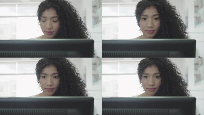 一位留着非洲头发的拉丁女性坐在办公室的电脑前，为客户工作