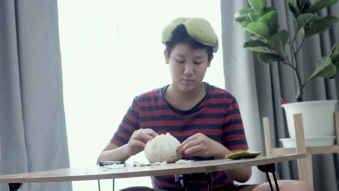 快乐的亚洲男孩坐在家窗户附近的地板上剥柚子，生活方式理念。