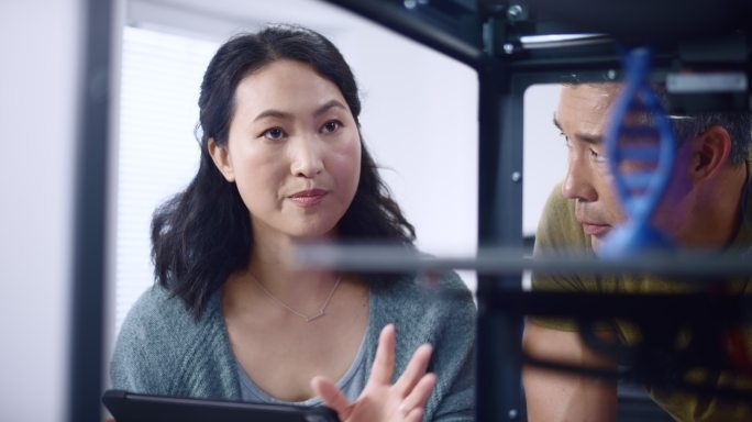 亚洲女工程师和她的亚洲男同事讨论在3D打印机中构建双螺旋模型