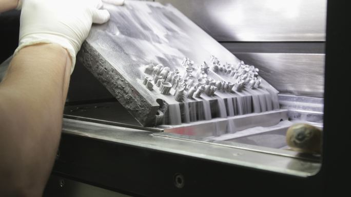 牙科技师在3D中用牙种植体从铸造板上倾倒金属粉末