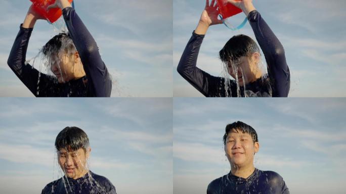 快乐的亚洲男孩在阳光明媚的日子把水桶倒在沙滩上，头上溅起水花，生活方式理念。