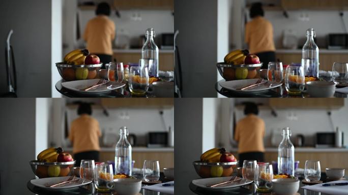 一位亚裔中国中年女性早上在厨房准备早餐，一边听着耳机的后视图