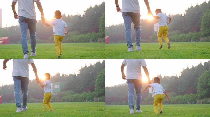 夕阳下爸爸牵着孩子的手在草地上散步-父子