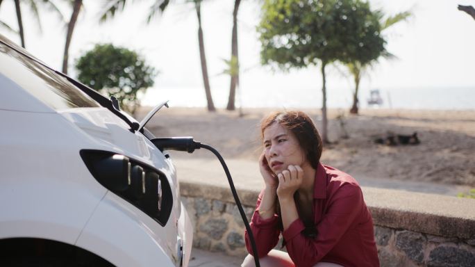 无聊的亚洲女人在等待电子汽车充电