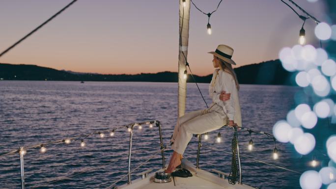 斯洛·莫（SLO-MO）时尚女性在帆船甲板上享受微风，甲板上用细绳灯照明
