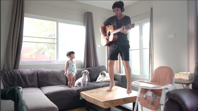快乐的父亲在家的客厅里和一个儿子和两只狗弹吉他。
