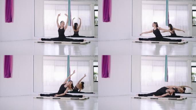 一位年轻的亚洲女性在有镜子的白色房间里，在瑜伽垫上以劈开的姿势伸展双腿。练习瑜伽锻炼身体的灵活性和伸