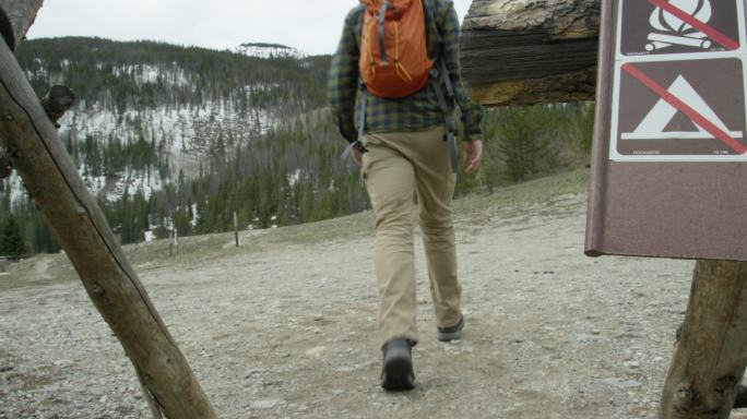 一名年轻的高加索男子背着背包，走过“禁止篝火”和“禁止露营”的路标，准备在冬季阴云密布的科罗拉多州落